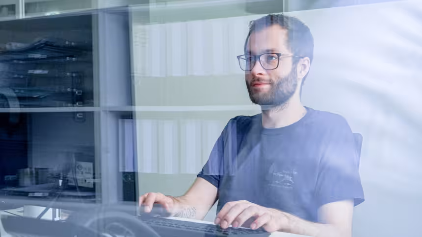 Eine Person sitzt an einem Schreibtisch vor einer Tastatur